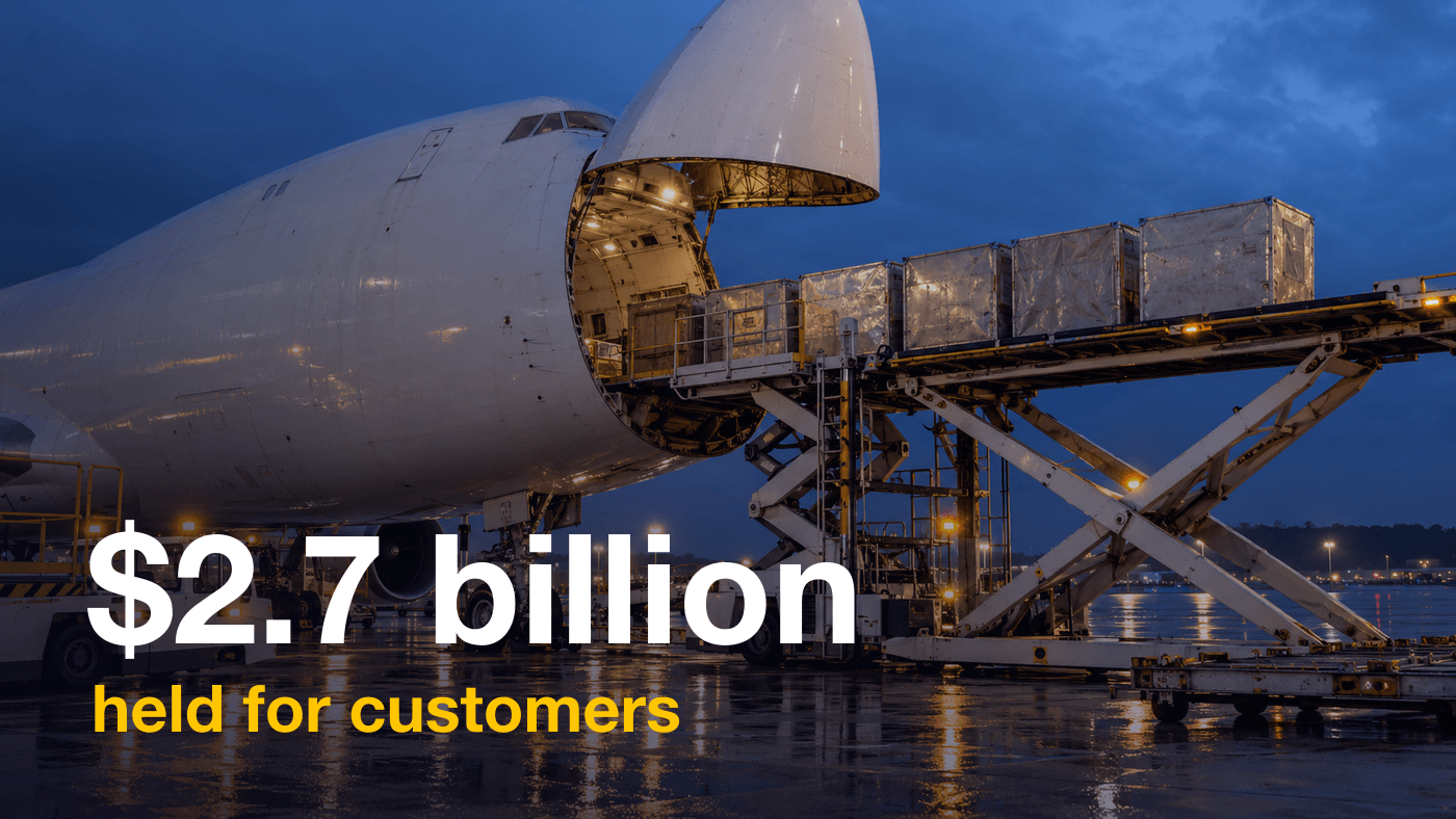 A white cargo jet with its nose door open at dusk as a loader lifts freight containers into the hold