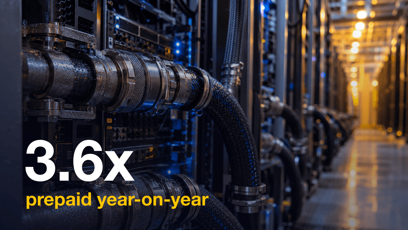 Liquid cooling pipes and braided hoses running along a row of server racks in a data center hall, lit in cool blue and warm amber